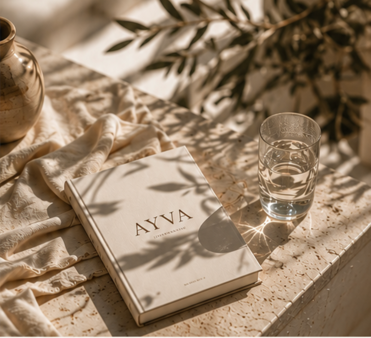 An AYVA book resting on a sunlit travertine ledge beside a vase and glass of water